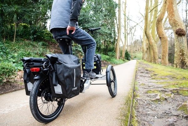 Fietser met beladen bagagedragers op een driewielige fiets op een bospad